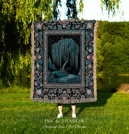 May include: A woven tapestry throw blanket with a black background and a detailed floral border. The center of the blanket features a dark blue willow tree with a crescent moon above it. The tree is surrounded by a dark blue path and a castle in the distance. The text 'INK & SHADOW Original Fine Art Throws' is printed below the blanket.
