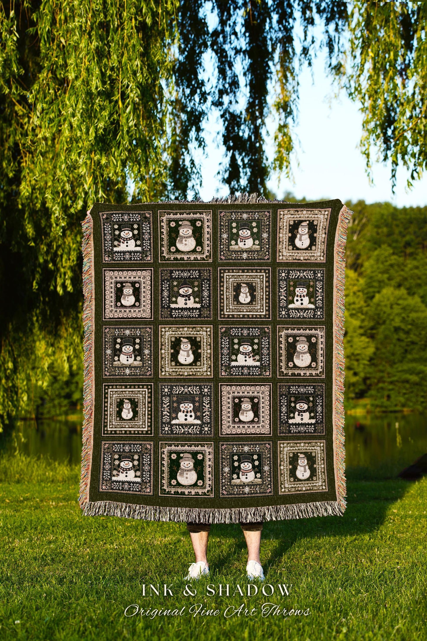 May include: A dark green woven throw blanket features a repeating pattern of framed snowmen. Each square contains a unique snowman design against a green background. The blanket has fringed edges.  The text 'INK & SHADOW Original Fine Art Throws' is visible at the bottom.