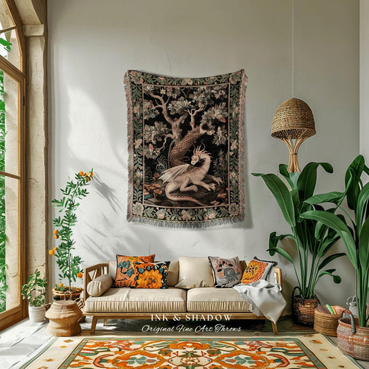 May include: A woven tapestry wall hanging featuring a white dragon with pink accents in a forest setting. The tapestry has a dark green, black, and pink color scheme. The tapestry is hanging on a white wall above a beige couch with throw pillows. The text 'INK & SHADOW Original Fine Art Throws' is visible below the couch.