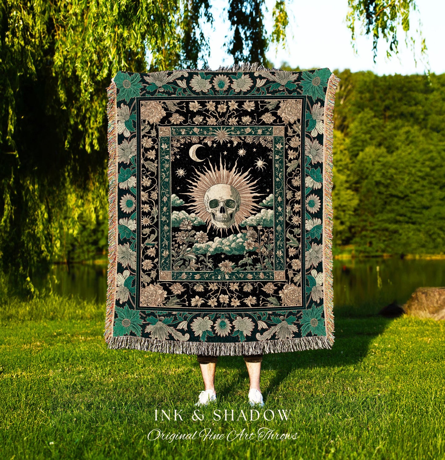 May include: A black throw blanket with a central design featuring a skull surrounded by a sunburst, moon, and stars. The blanket has a floral border with green and tan accents, and the text "INK & SHADOW Original Fine Art Throws" is at the bottom.