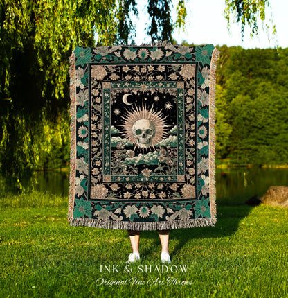 May include: A black throw blanket with a central design featuring a skull surrounded by a sunburst, moon, and stars. The blanket has a floral border with green and tan accents, and the text "INK & SHADOW Original Fine Art Throws" is at the bottom.