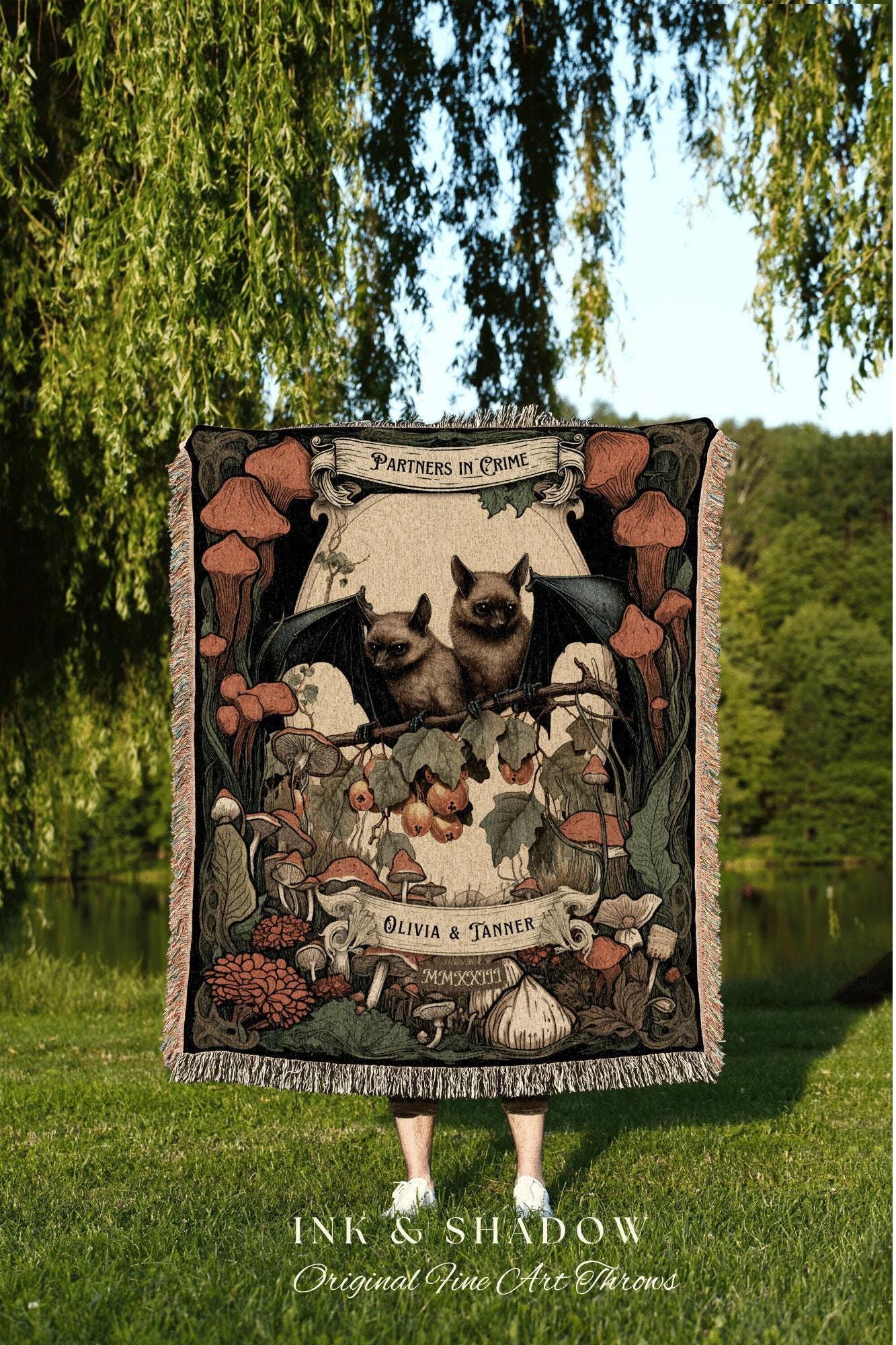 May include: A woven tapestry with a dark background featuring two bats with wings spread, perched on a branch with red berries and mushrooms. The tapestry has a banner at the top that reads 'Partners in Crime' and a banner at the bottom that reads 'Olivia & Tanner.' The tapestry is framed with a black border and has a fringe around the edges. The tapestry is a dark green, black, and red color.