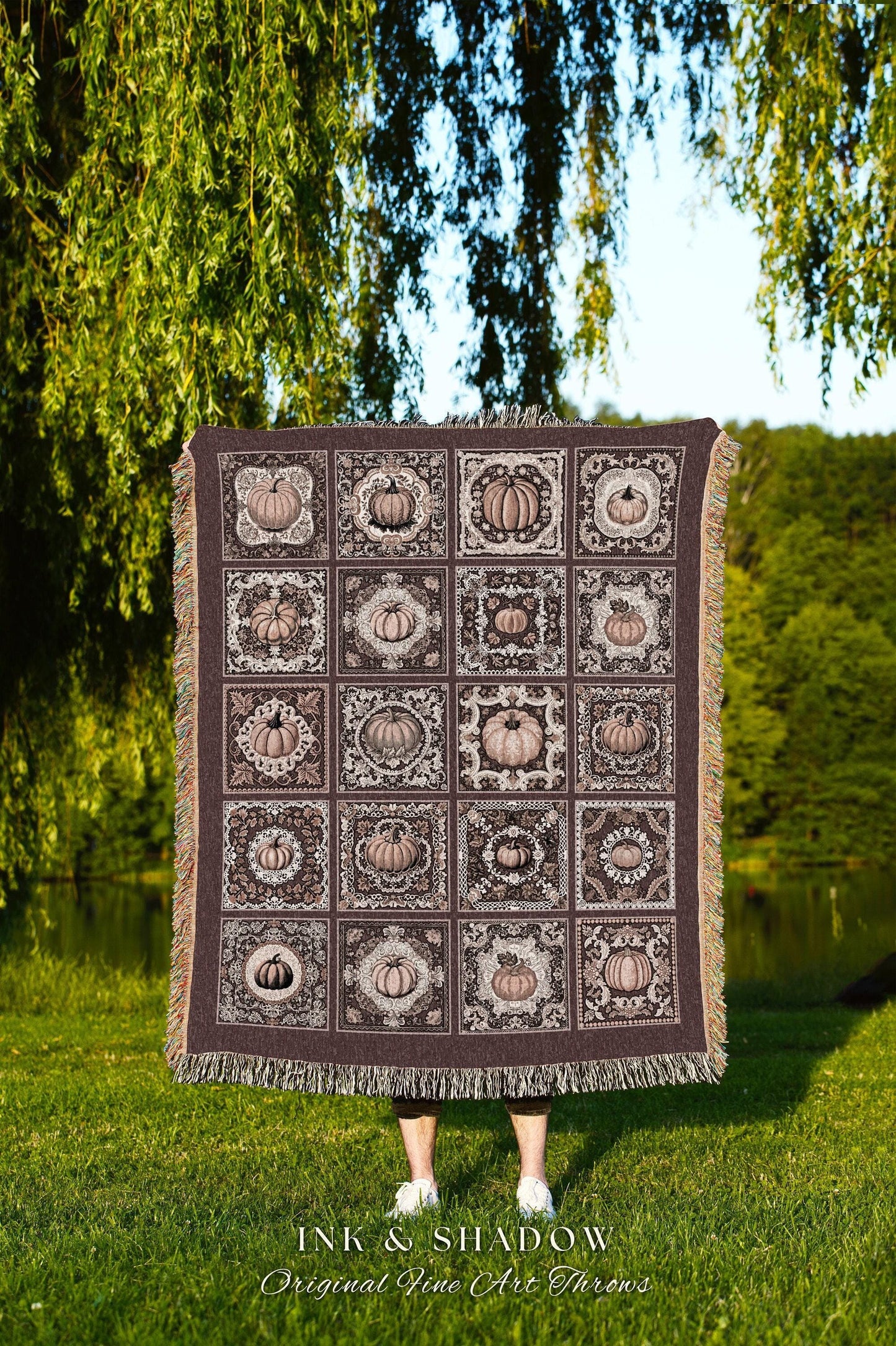 May include: A woven throw blanket with a brown background and a pattern of beige pumpkins in decorative frames. The text 'INK & SHADOW Original Fine Art Throws' is at the bottom of the blanket.