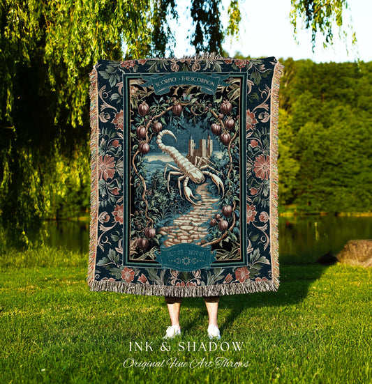 May include: A woven tapestry throw blanket with a dark blue background. The blanket features a white scorpion with a dark blue tail and a dark blue castle in the background. The blanket has a floral border with pink, white, and green flowers. The text on the blanket reads 'SCORPIO - THE SCORPION' and 'OCT 23 - NOV 21'. The text 'INK & SHADOW Original Fine Art Throws' is printed below the blanket.