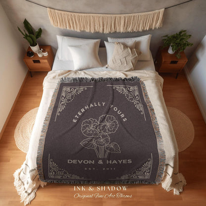 May include: A woven throw blanket with a dark gray background and white text and design. The text reads 'Eternally Yours', 'Devon & Hayes', 'Est. 2011', 'Ink & Shadow', and 'Original Fine Art Throws'. The design features a stylized floral motif.