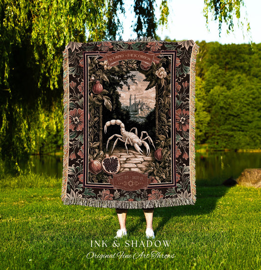 May include: A woven tapestry throw blanket with a dark brown background and a floral border. The center of the blanket features a white scorpion with a dark brown body and a light brown tail. The scorpion is standing on a path with a city in the background. The text 'SCORPIO - THE SCORPION' is written in a banner above the scorpion. The text 'OCT 23 - NOV 21' is written in a banner below the scorpion. The blanket is made by Ink & Shadow Original Fine Art Throws.