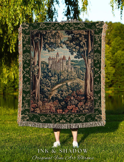 May include: A tapestry throw blanket featuring a castle scene with trees and a winding road. The blanket has a green border with floral designs and fringe. The text "INK & SHADOW Original Fine Art Throws" is at the bottom.