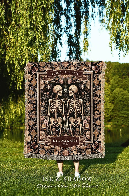 May include: A black and brown throw blanket featuring a floral and skeleton design. The blanket has the words "Kindred Spirits" and "Dylan & Gabby 2024" on it. The bottom of the blanket has the words "INK & SHADOW Original Fine Art Throws".