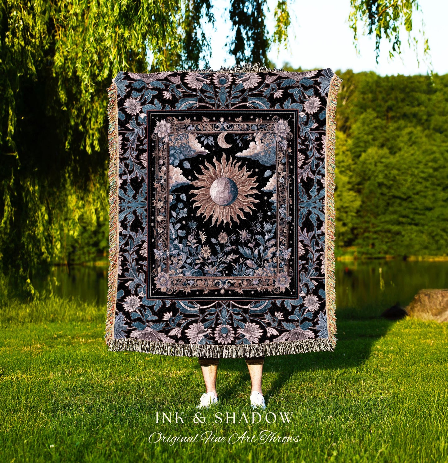 May include: A decorative throw blanket with a celestial design featuring a sun, moon, and floral elements. The blanket has a black background with teal and beige accents, and a fringed edge. The text "INK & SHADOW Original Fine Art Throws" is at the bottom.