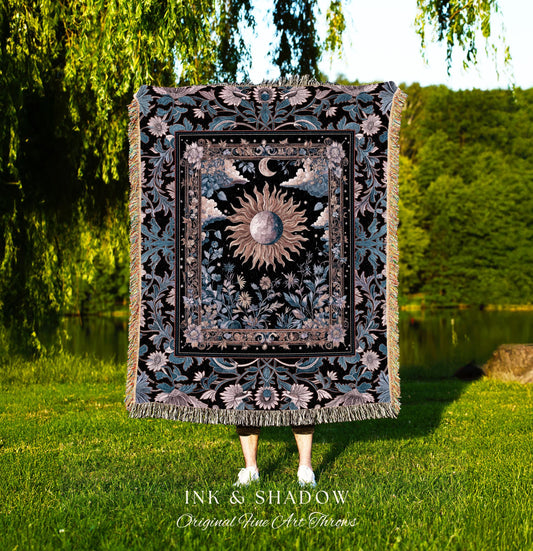 May include: A decorative throw blanket with a celestial design featuring a sun, moon, and floral elements. The blanket has a black background with teal and beige accents, and a fringed edge. The text "INK & SHADOW Original Fine Art Throws" is at the bottom.
