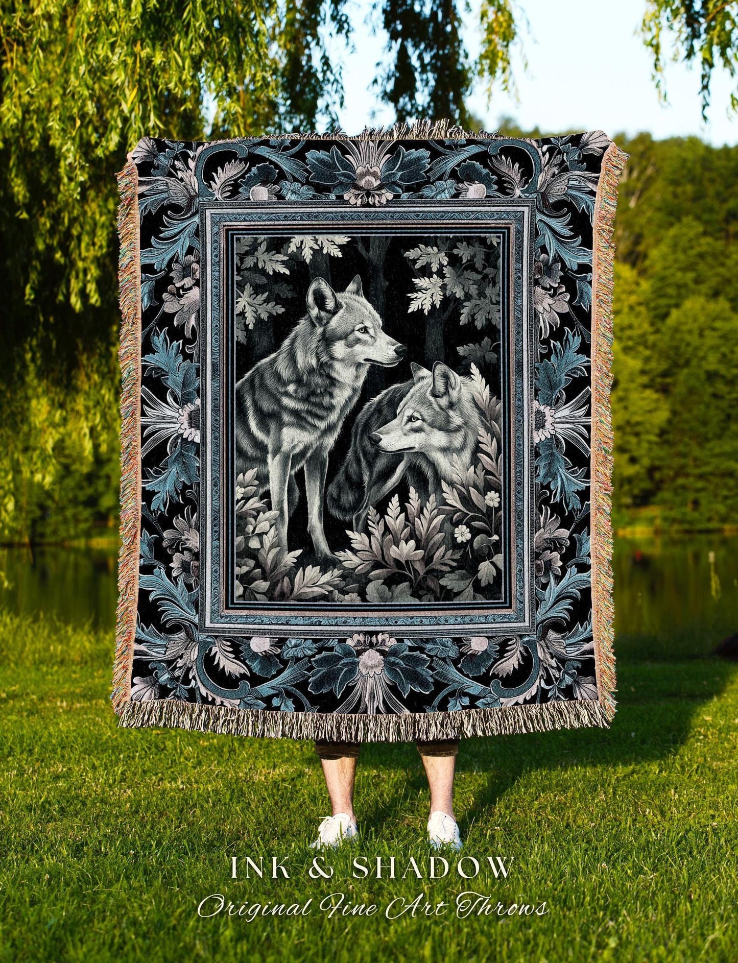 May include: A black and teal throw blanket featuring a framed image of two wolves in a forest setting. The blanket has a decorative border with floral and leaf patterns and a fringed edge. The text "INK & SHADOW Original Fine Art Throws" is at the bottom.