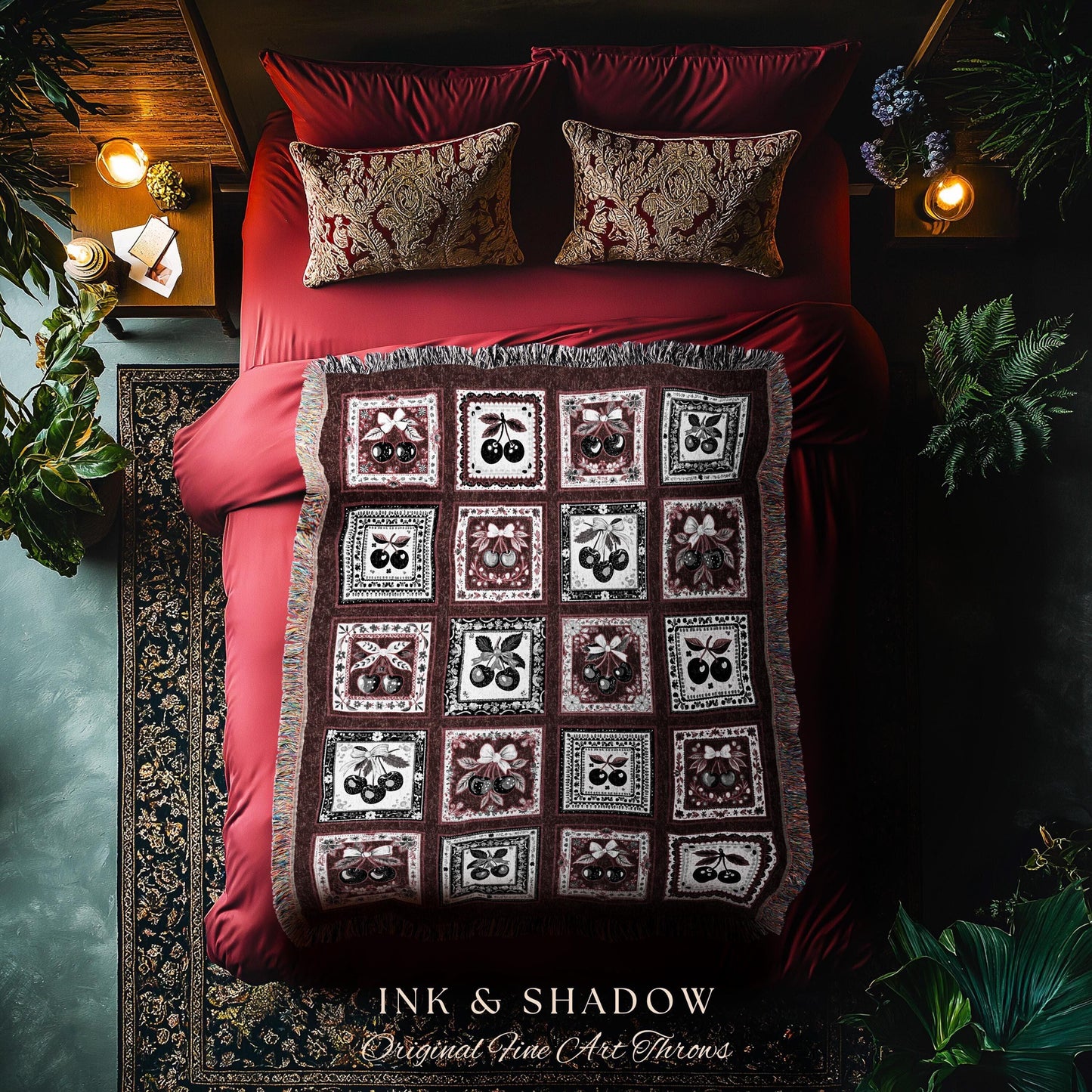 May include: A red throw blanket with a pattern of black cherries in a white frame on a burgundy background. The blanket is on a red bed with two pillows with a gold and white pattern. The text 'INK & SHADOW Original Fine Art Throws' is at the bottom of the image.