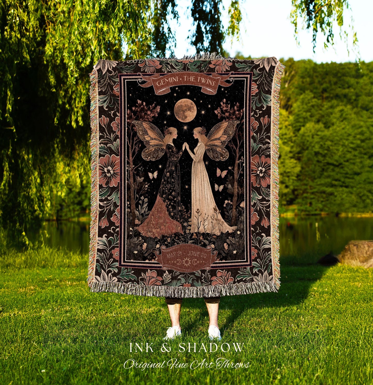 May include: A woven tapestry throw blanket with a dark background featuring two fairies with wings. The fairies are standing in a forest with a full moon and stars in the sky. The text on the blanket reads 'Gemini, The Twins' and 'May 21st - June 20th'. The blanket has a dark green, black, and brown color scheme with pink flowers on the border.