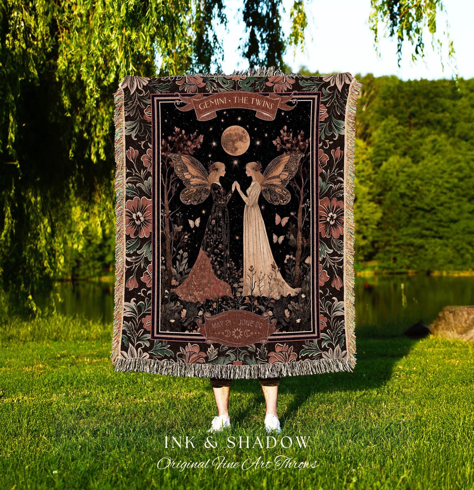 May include: A woven tapestry throw blanket with a dark background featuring two fairies with wings. The fairies are standing in a forest with a full moon and stars in the sky. The text on the blanket reads 'Gemini, The Twins' and 'May 21st - June 20th'. The blanket has a dark green, black, and brown color scheme with pink flowers on the border.