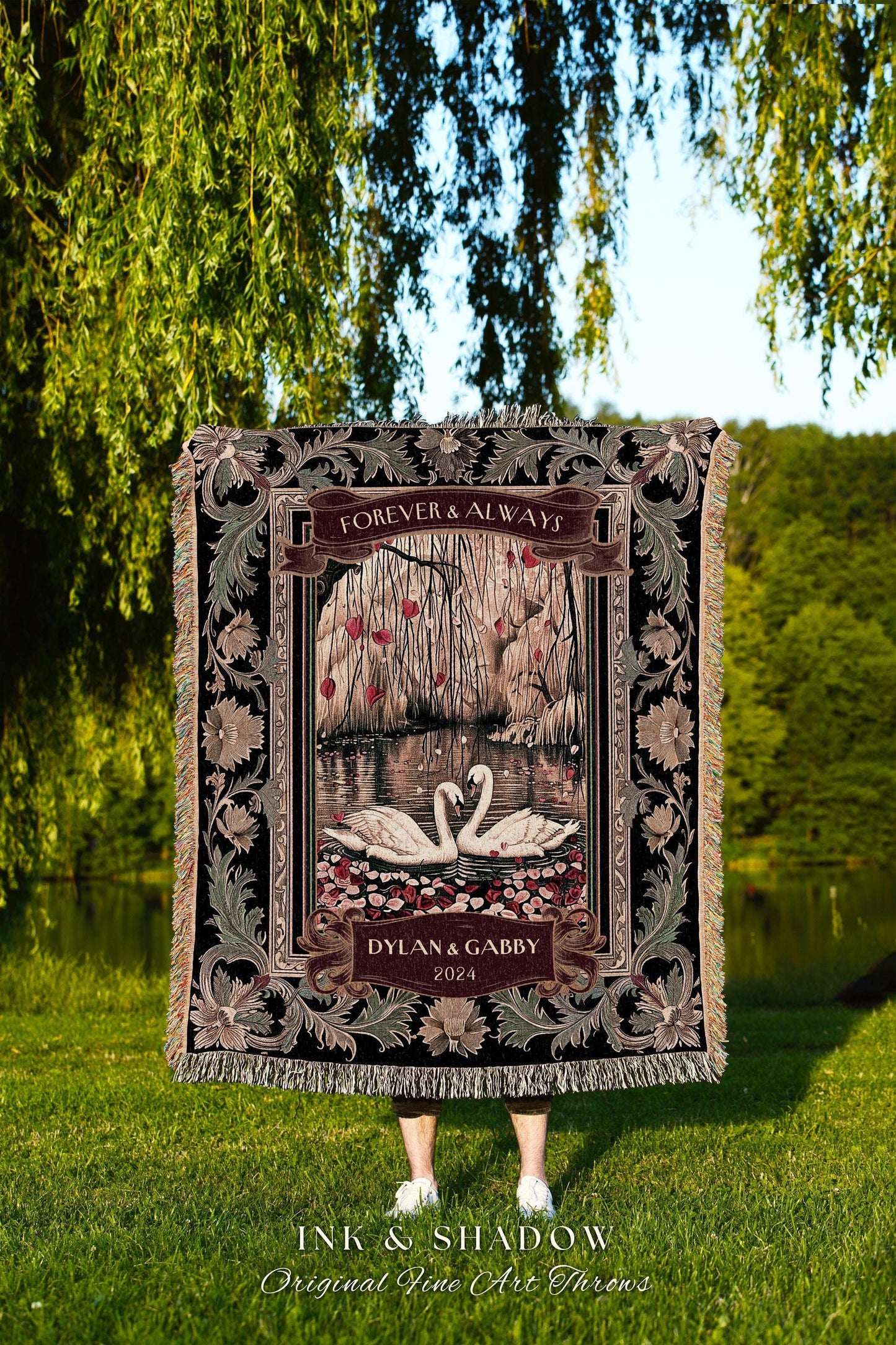 May include: A black tapestry throw blanket with a floral border. The center of the blanket features a pair of white swans on a lake with a willow tree in the background. The text 'Forever & Always' is above the swans and the text 'Dylan & Gabby 2024' is below the swans. The blanket is made by Ink & Shadow Original Fine Art Throws.