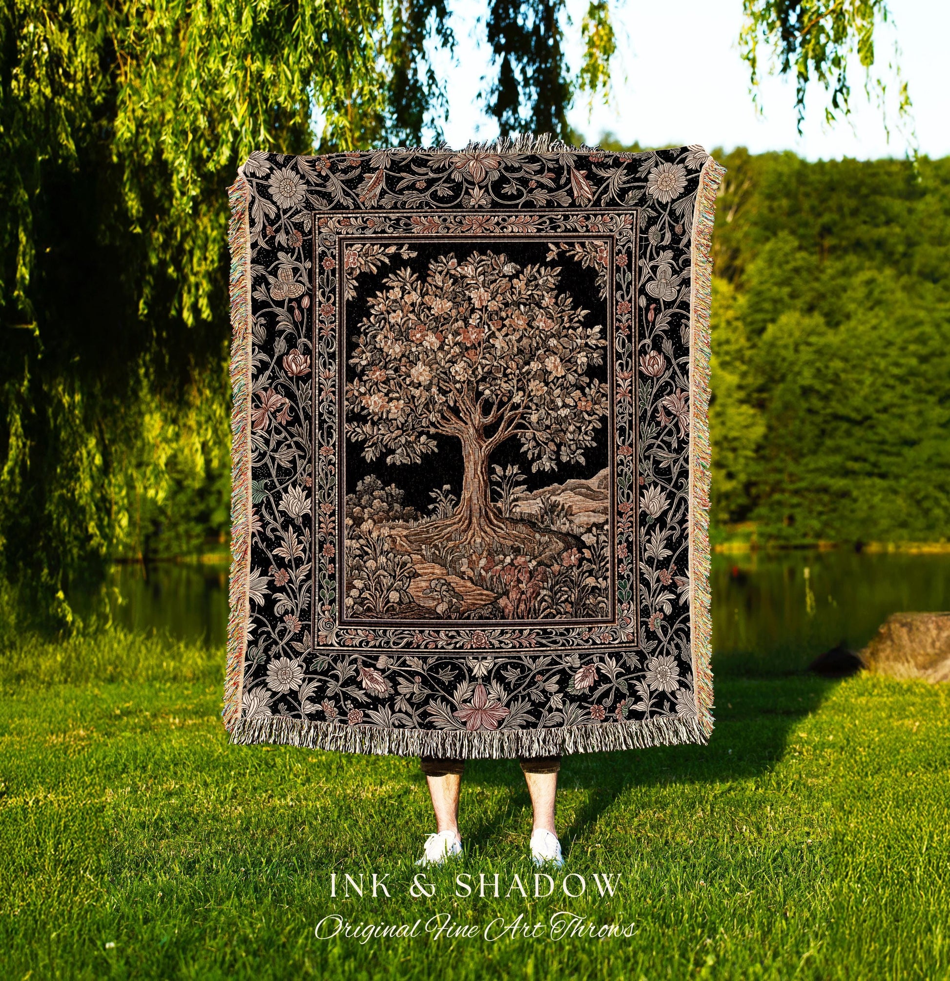 May include: A black throw blanket with a detailed tree design, framed by floral patterns and fringe. The tree has a large trunk and branches with leaves. The blanket has the text "INK & SHADOW Original Fine Art Throws".
