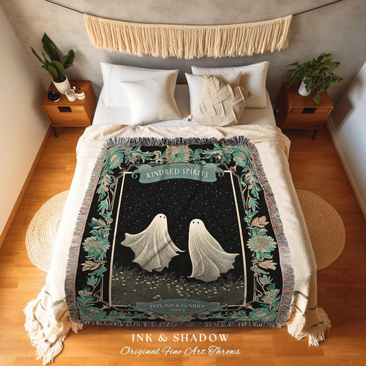 May include: A woven tapestry throw blanket with a black background and a white frame. The center of the blanket features two white ghosts with black eyes. The text 'Kindred Spirits 2024' is above the ghosts and the text 'Dylan & Gabby' is below the ghosts. The bottom of the blanket has the text 'Ink & Shadow Original Fine Art Throws'.