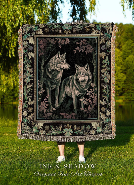 May include: A woven throw blanket featuring a detailed illustration of two wolves in a forest setting. The blanket has a dark background with floral and leaf border designs in shades of green, pink, and beige. The text "INK & SHADOW Original Fine Art Throws" is at the bottom.