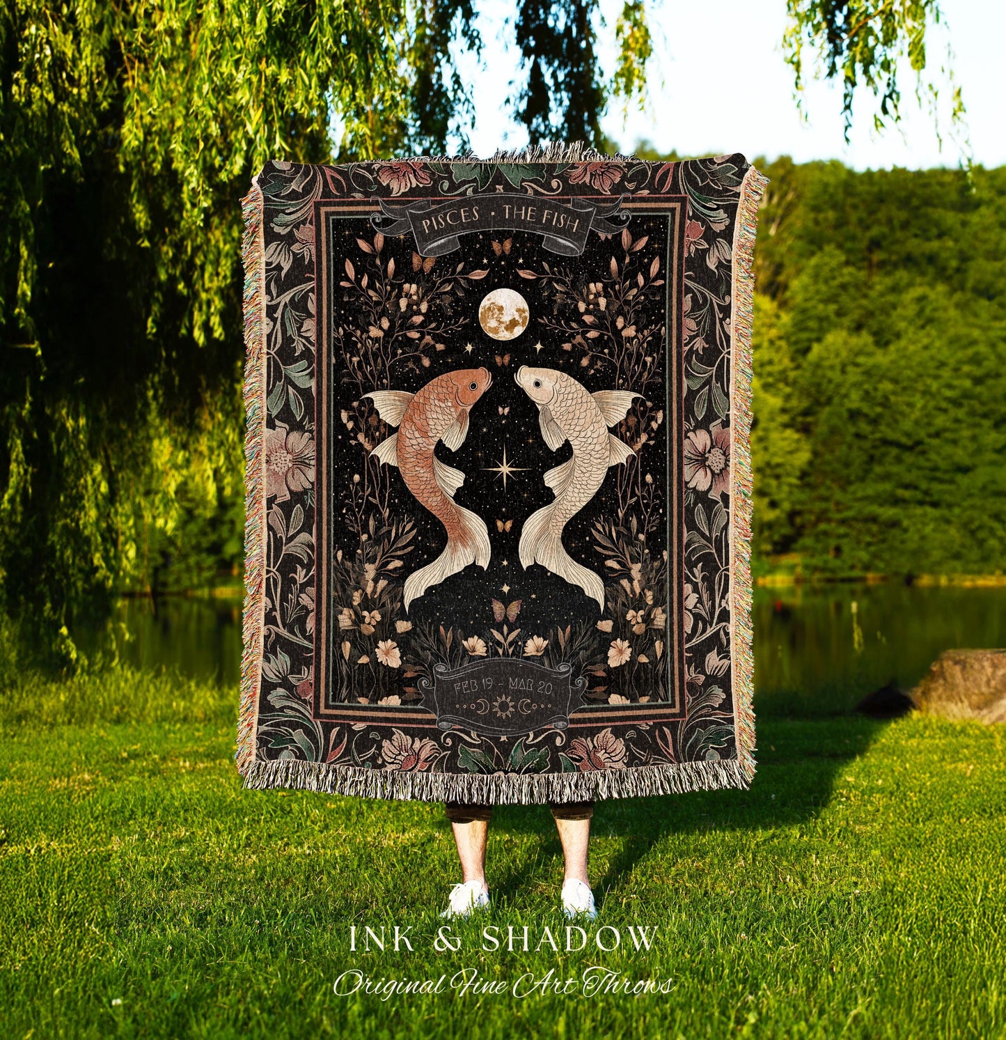 May include: A black woven throw blanket with a floral design and two gold fish. The blanket has a black border with the text 'PISCES THE FISH' and 'FEB 19-MAR 20' in white. The blanket is displayed in front of a green grassy background. The text 'INK & SHADOW Original Fine Art Throws' is displayed below the blanket.