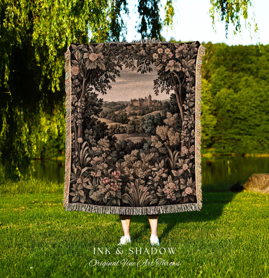 May include: A decorative throw blanket with a detailed landscape scene featuring a castle, trees, and flowers in shades of brown, black, and beige. The blanket has a fringed edge and the text "INK & SHADOW Original Fine Art Throws" at the bottom.