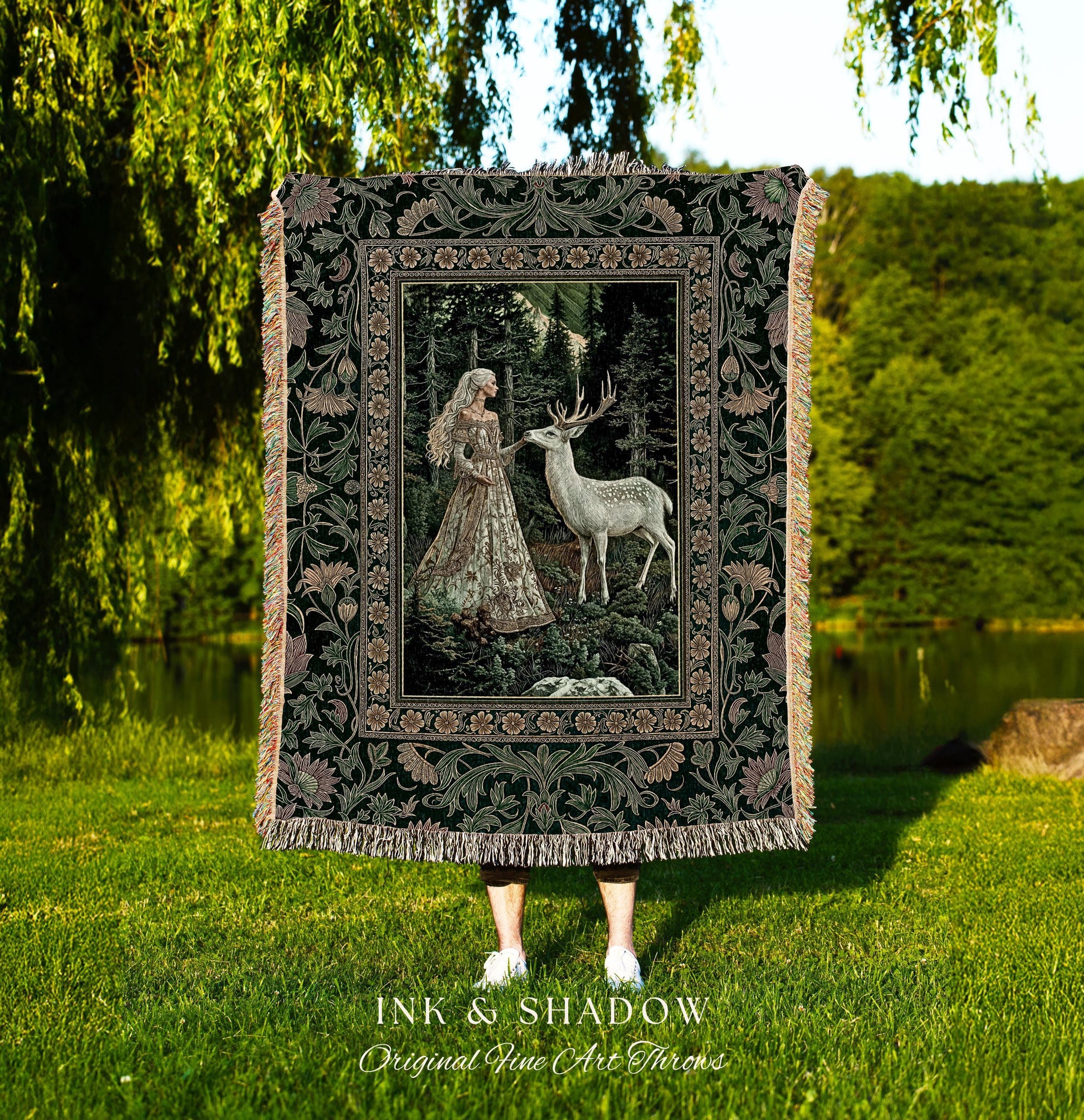 May include: A tapestry throw blanket featuring a forest scene with a woman and a deer. The blanket has a dark green floral border and fringe. The text "INK & SHADOW Original Fine Art Throws" is at the bottom.