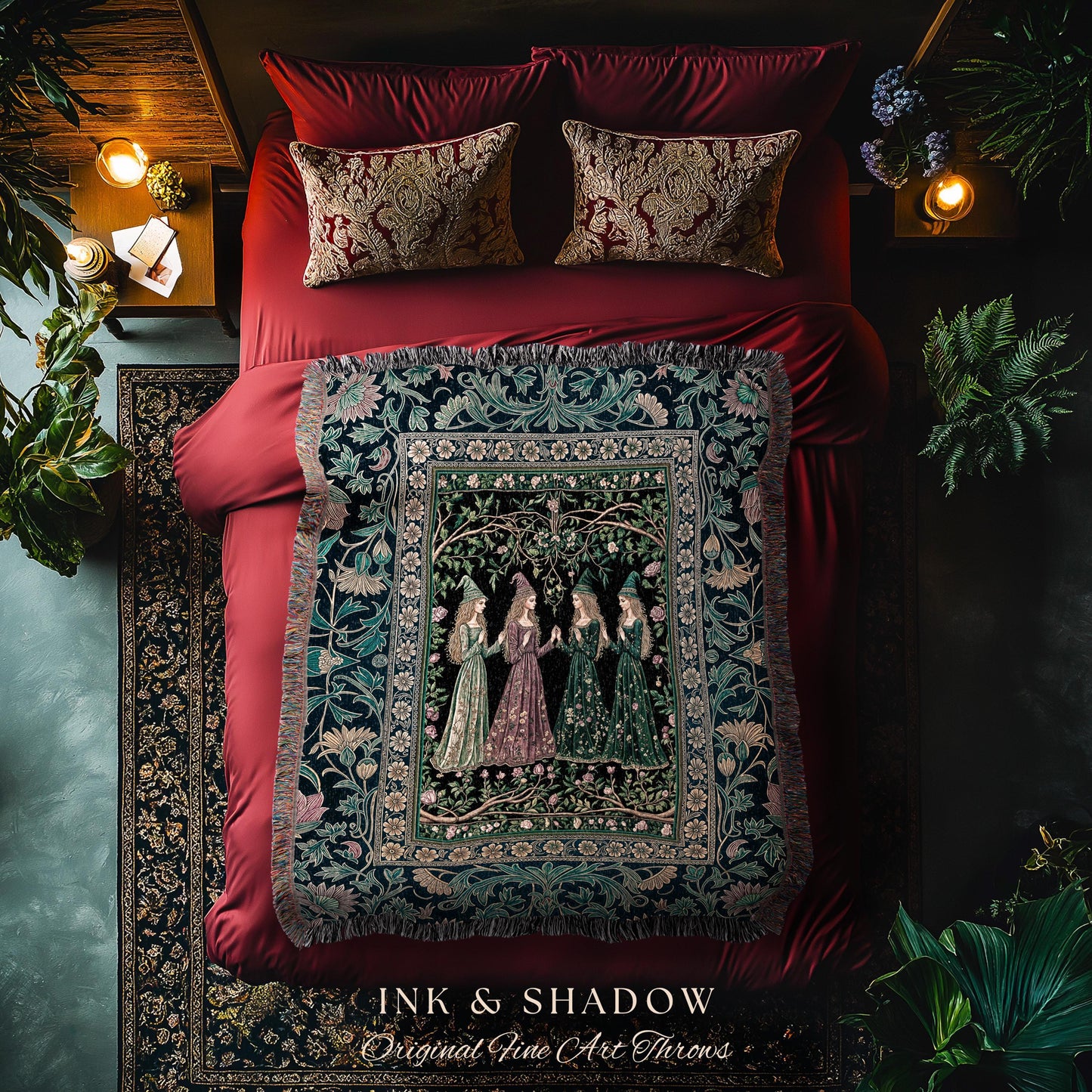 May include: A bed with red bedding, patterned pillows, and a decorative throw blanket. The throw features a detailed illustration of women in gowns. The text "INK & SHADOW Original Fine Art Throws" is at the bottom.