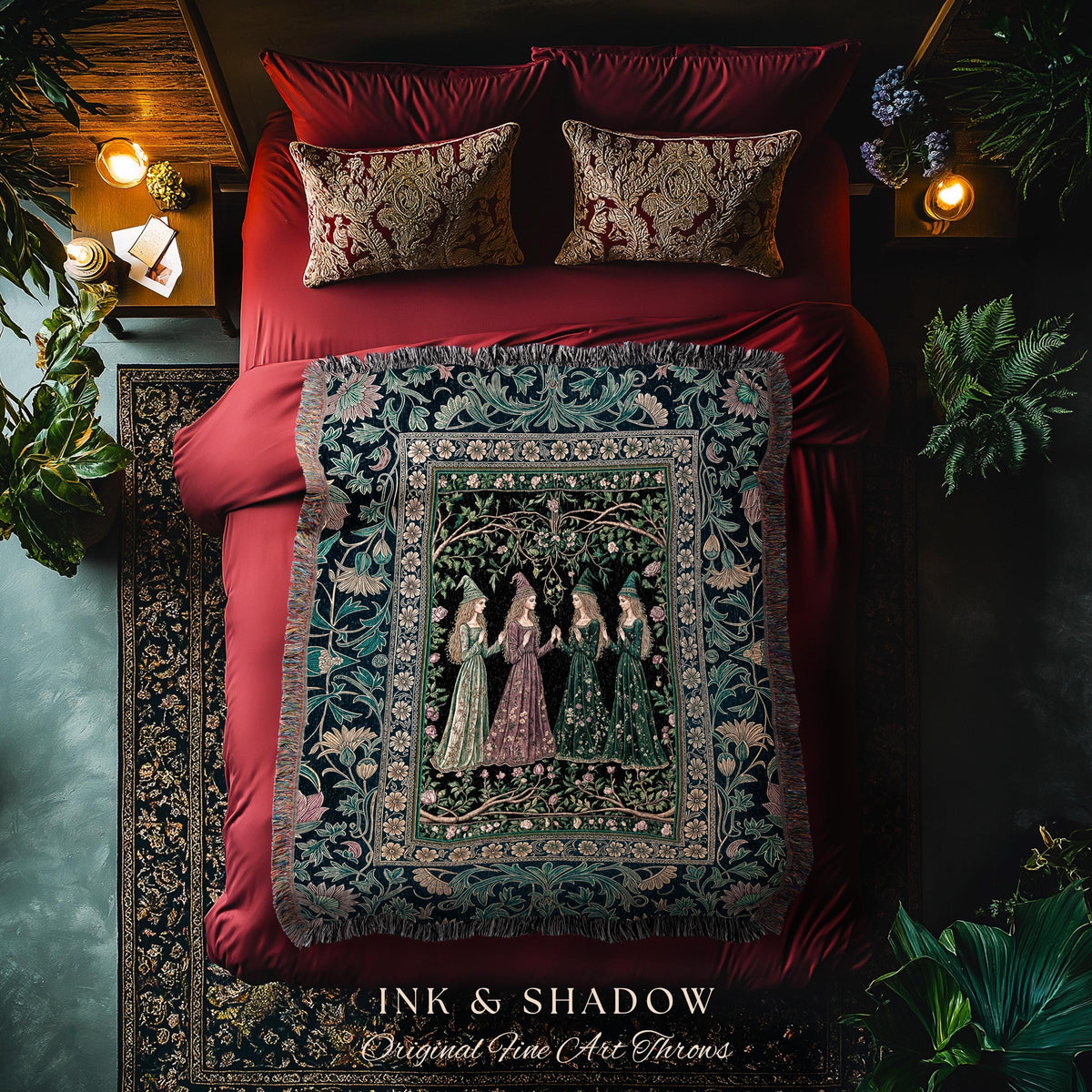 May include: A bed with red bedding, patterned pillows, and a decorative throw blanket. The throw features a detailed illustration of women in gowns. The text "INK & SHADOW Original Fine Art Throws" is at the bottom.