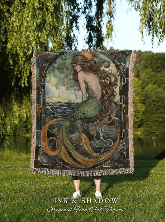 May include: A woven throw blanket featuring a mermaid illustration in shades of green, blue, and gold. The artwork depicts a mermaid with long flowing hair, seated near water. The blanket has a fringed edge and the text "INK & SHADOW Original Fine Art Throws".