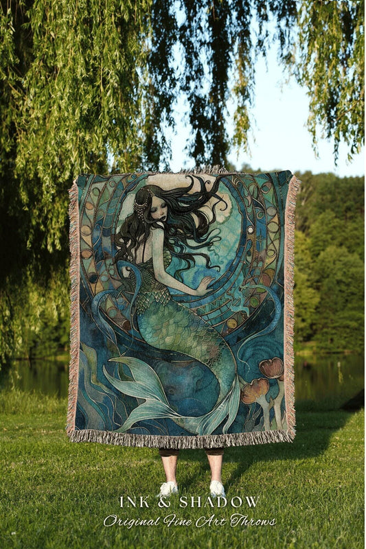May include: A woven throw blanket featuring a mermaid illustration in shades of teal, blue, and green. The mermaid has long black hair and is surrounded by aquatic elements. The blanket has a fringed edge and the text "INK & SHADOW Original Fine Art Throws".