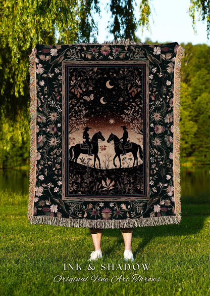May include: A dark green throw blanket with a detailed illustration of two riders on horseback under a night sky with moons and stars. The blanket has a floral border and fringe. The text "INK & SHADOW Original Fine Art Throws" is at the bottom.