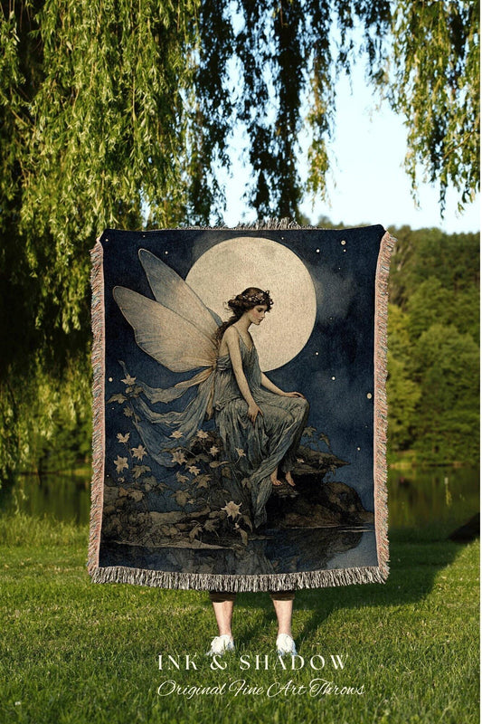 May include: A dark blue throw blanket featuring a fairy with large wings, seated in front of a full moon. The artwork has a vintage aesthetic, with a fringe border. The text "INK & SHADOW Original Fine Art Throws" is at the bottom.