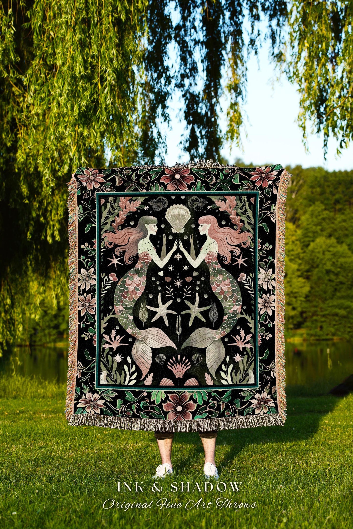 May include: A black throw blanket with a mermaid design. The blanket features two mermaids with pink hair and green tails, surrounded by starfish, shells, and floral elements. The text "INK & SHADOW Original Fine Art Throws" is at the bottom.