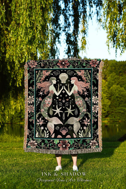 May include: A black throw blanket with a mermaid design. The blanket features two mermaids with pink hair and green tails, surrounded by starfish, shells, and floral elements. The text "INK & SHADOW Original Fine Art Throws" is at the bottom.