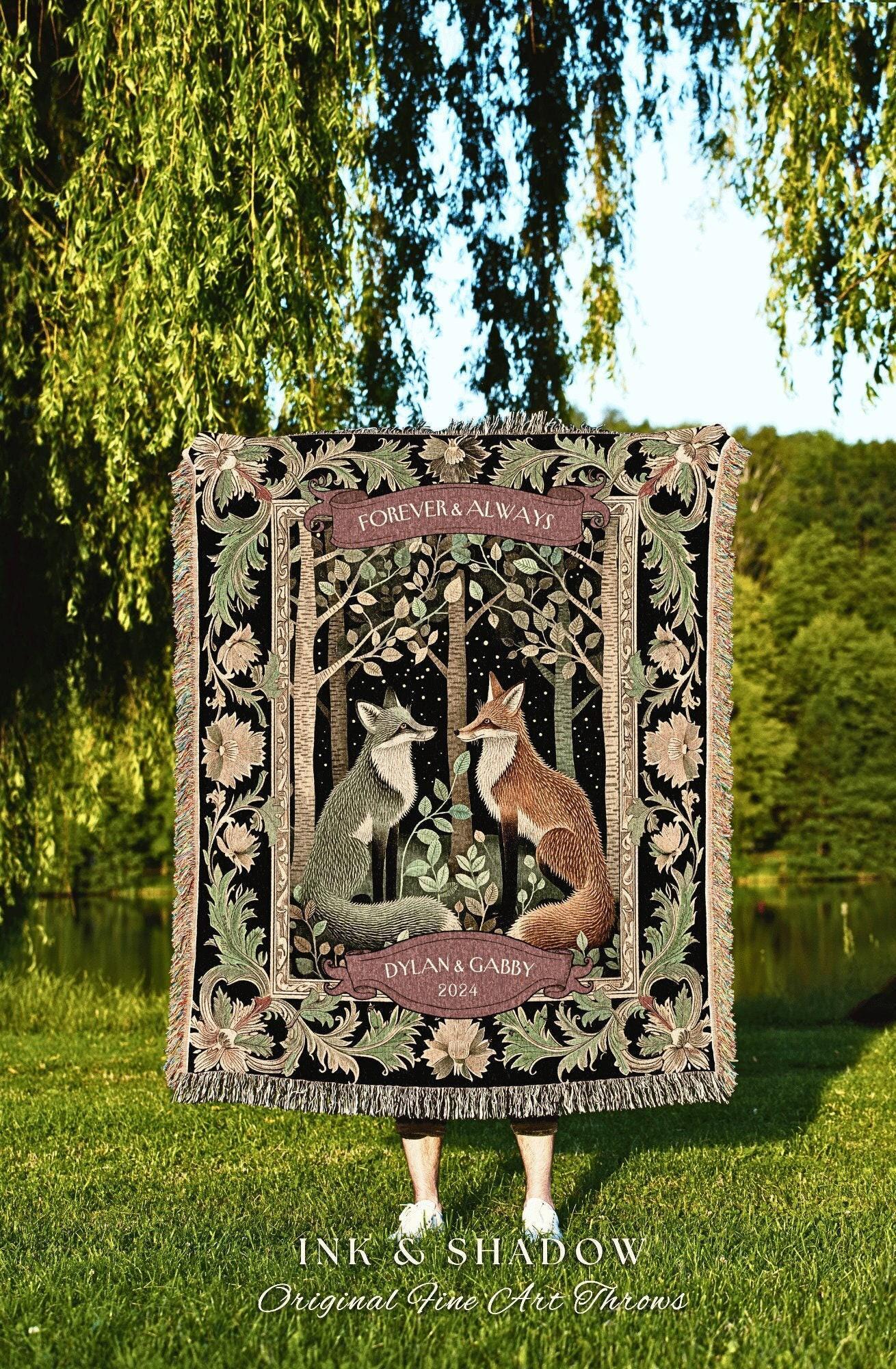 May include: A woven throw blanket featuring a forest scene with two foxes facing each other. The blanket has a black background with floral and leaf accents. Text includes "FOREVER & ALWAYS" and "DYLAN & GABBY 2024". The blanket is fringed.