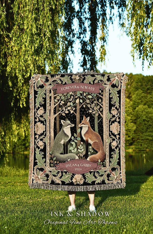May include: A woven throw blanket featuring a forest scene with two foxes facing each other. The blanket has a black background with floral and leaf accents. Text includes "FOREVER & ALWAYS" and "DYLAN & GABBY 2024". The blanket is fringed.