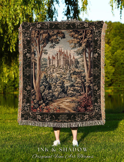 May include: A tapestry throw blanket featuring a detailed landscape scene with a castle, trees, and a path. The blanket has a black border with floral designs and fringe. The text "INK & SHADOW Original Fine Art Throws" is at the bottom.