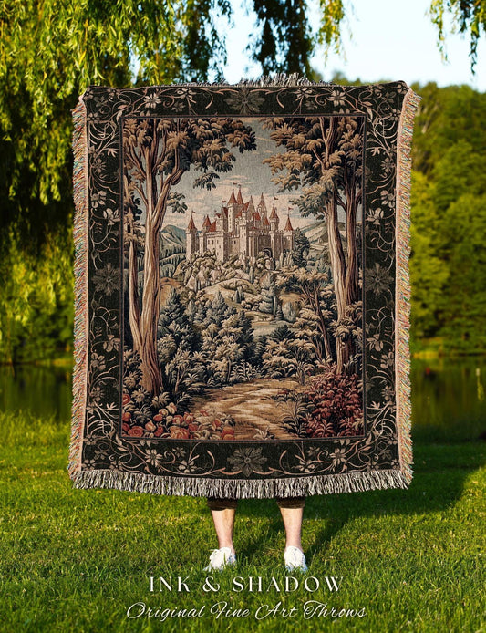 May include: A tapestry throw blanket featuring a detailed landscape scene with a castle, trees, and a path. The blanket has a black border with floral designs and fringe. The text "INK & SHADOW Original Fine Art Throws" is at the bottom.
