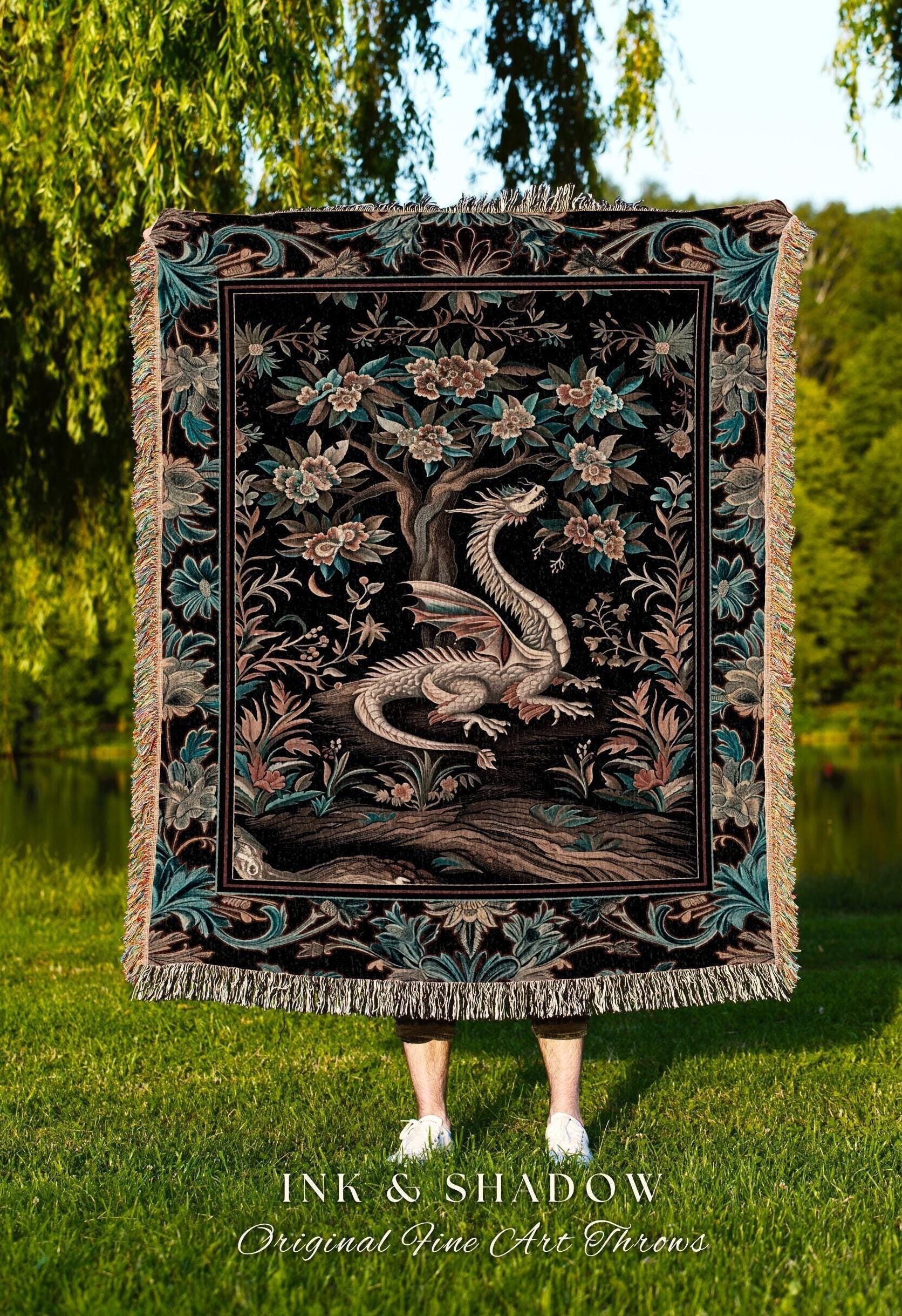 May include: A black tapestry throw blanket featuring a detailed illustration of a dragon resting beneath a flowering tree. The throw has a decorative border with floral and leaf patterns, and fringed edges. The text "INK & SHADOW Original Fine Art Throws" is at the bottom.