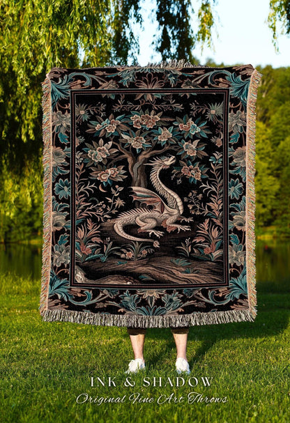 May include: A black tapestry throw blanket featuring a detailed illustration of a dragon resting beneath a flowering tree. The throw has a decorative border with floral and leaf patterns, and fringed edges. The text "INK & SHADOW Original Fine Art Throws" is at the bottom.