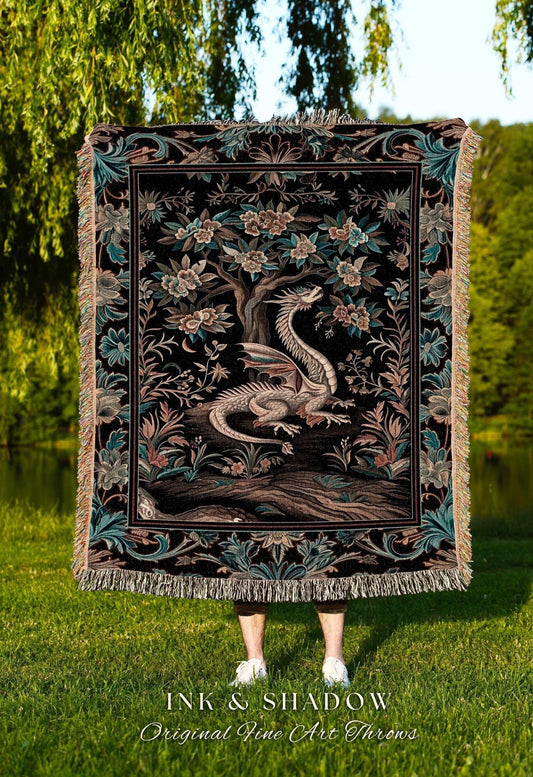May include: A black tapestry throw blanket featuring a detailed illustration of a dragon resting beneath a flowering tree. The throw has a decorative border with floral and leaf patterns, and fringed edges. The text "INK & SHADOW Original Fine Art Throws" is at the bottom.