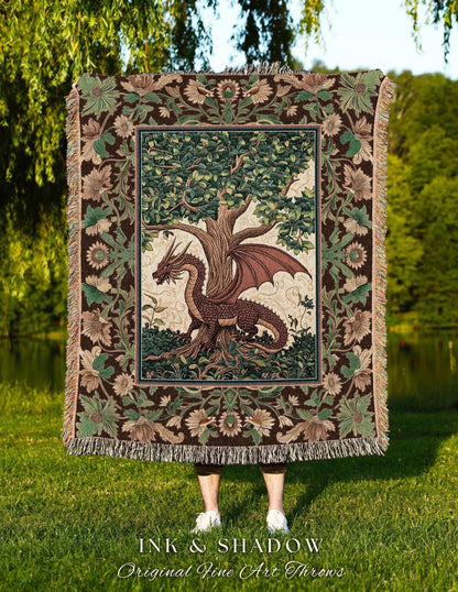 May include: A tapestry throw blanket featuring a dragon and tree design. The dragon is brown with red wings, and the tree has green leaves. The border is brown with floral and leaf patterns. The blanket has a fringed edge. The text "INK & SHADOW Original Fine Art Throws" is at the bottom.