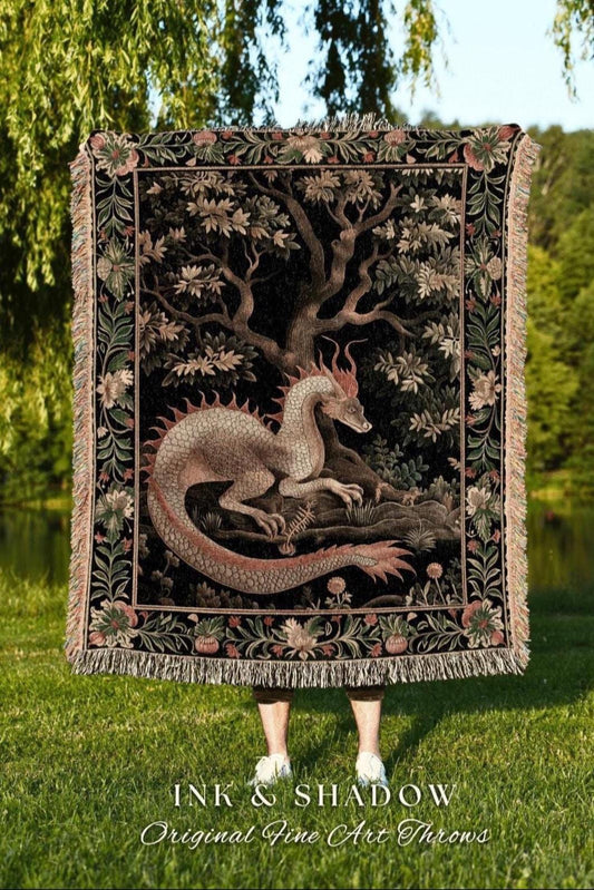 May include: A black throw blanket featuring a dragon illustration under a tree. The dragon is light brown with red accents. The blanket has a floral border and fringe. Text at the bottom reads "INK & SHADOW Original Fine Art Throws."
