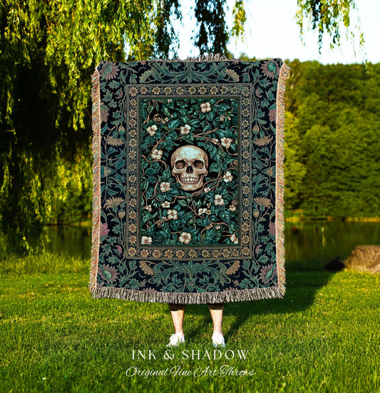 May include: A dark green throw blanket with a floral and skull design. The center features a skull surrounded by white flowers and green leaves. The blanket has a fringed edge and the text "INK & SHADOW Original Fine Art Throws" at the bottom.