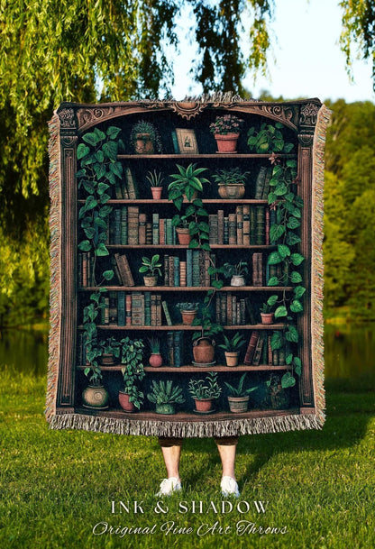 May include: A tapestry throw blanket featuring a detailed illustration of a bookshelf filled with books and potted plants. The design includes a dark brown frame and is fringed on the edges. The text "INK & SHADOW Original Fine Art Throws" is at the bottom.