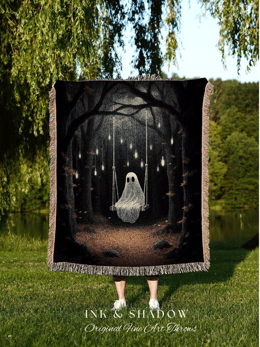 May include: Black throw blanket featuring a whimsical illustration of a ghost on a swing in a dark forest, illuminated by hanging lights. The blanket has a fringed edge and the text "INK & SHADOW Original Fine Art Throws".