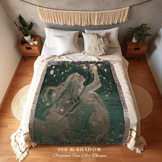 May include: A woven throw blanket featuring a mermaid design in shades of teal, green, and white. The artwork depicts a mermaid reaching upwards towards glowing stars. The blanket has a fringed edge and the text "INK & SHADOW Original Fine Art Throws".