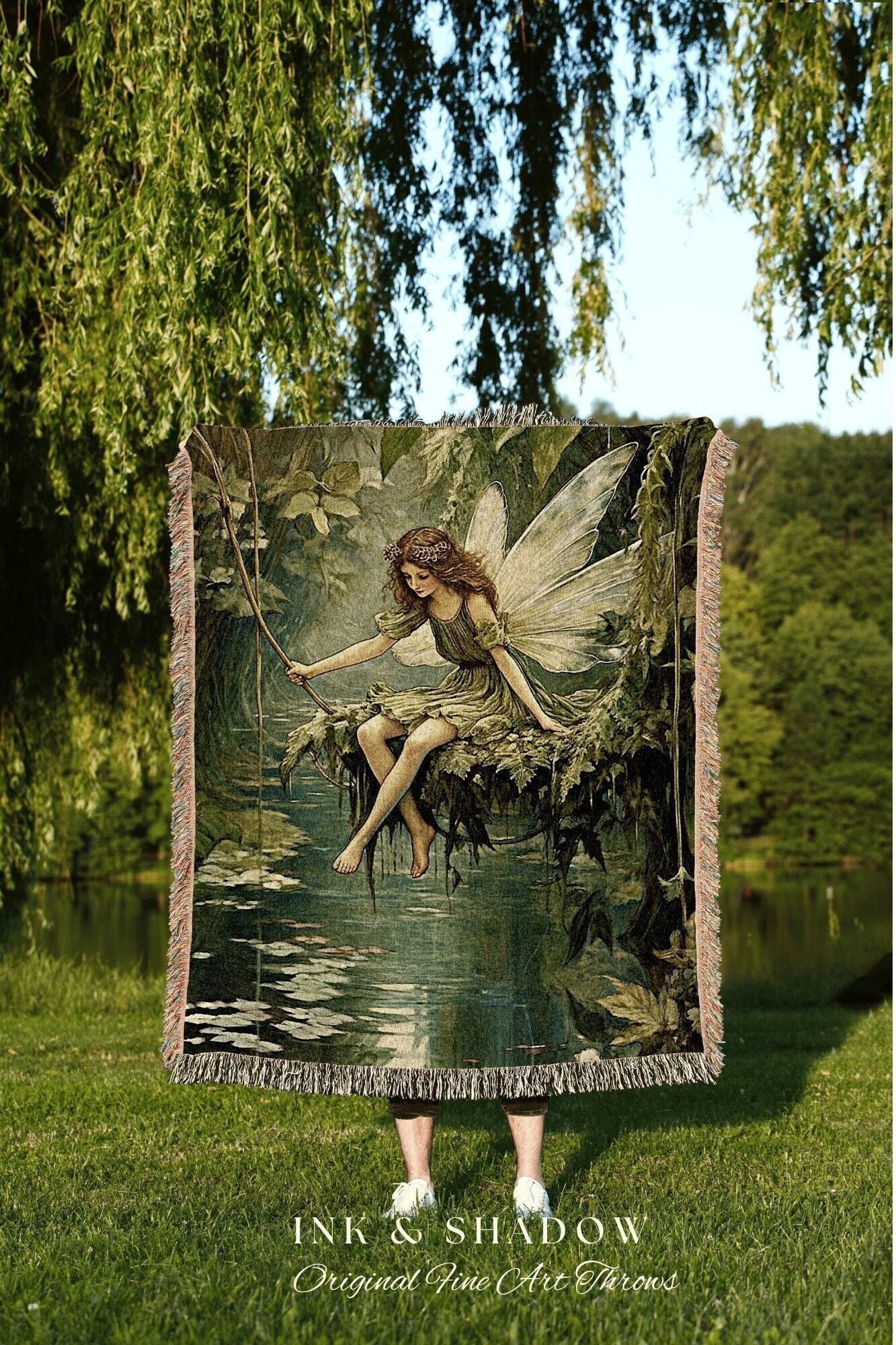 May include: A woven tapestry throw blanket featuring a fairy sitting on a tree branch over water. The artwork is in shades of green and brown, with a fringe border. The text "INK & SHADOW Original Fine Art Throws" is at the bottom.