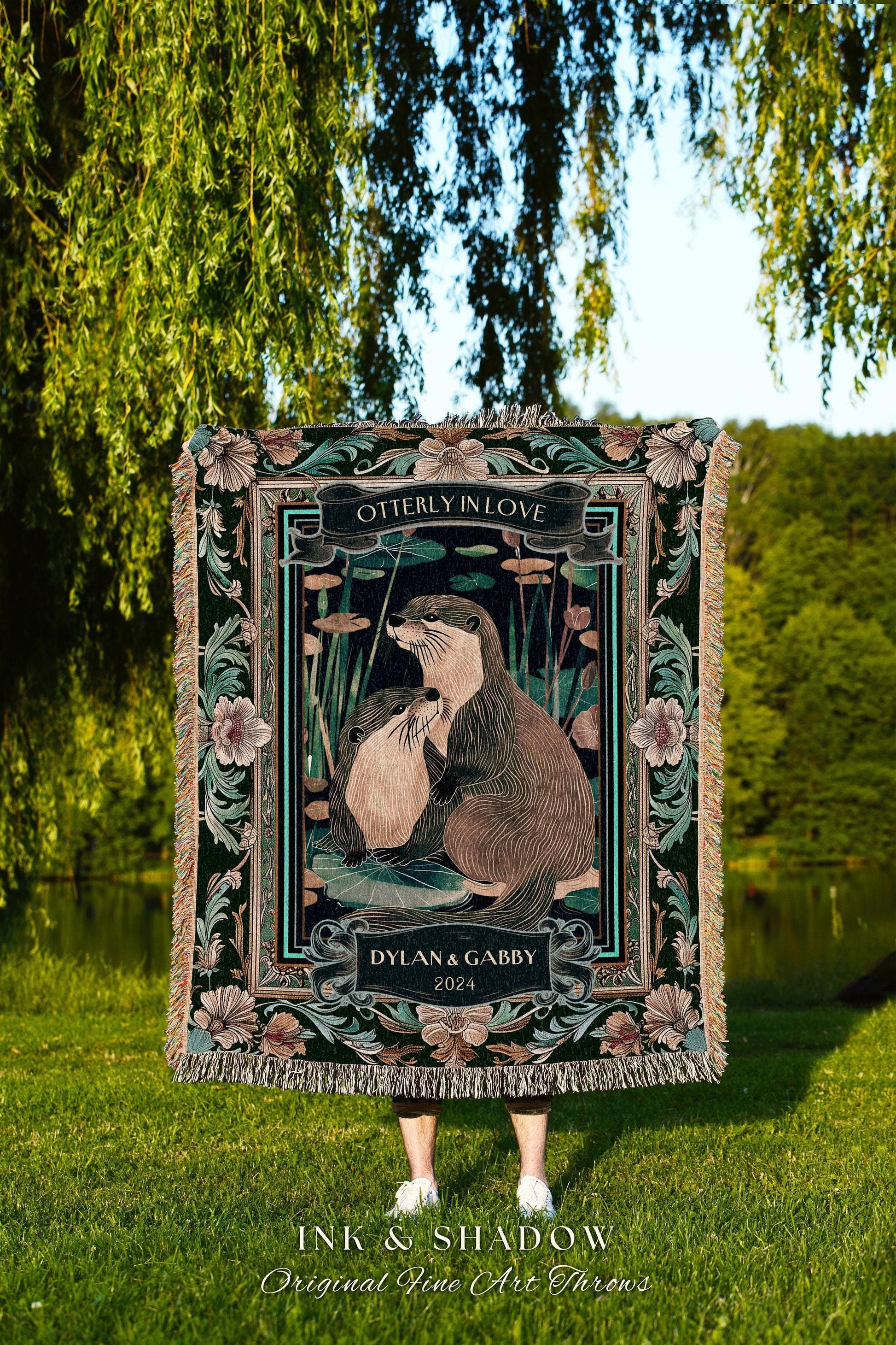 May include: A decorative throw blanket featuring an illustration of two otters in a pond, with the text "OTTERLY IN LOVE" and "DYLAN & GABBY 2024". The blanket has a dark green background with floral and leaf accents and a fringed edge.