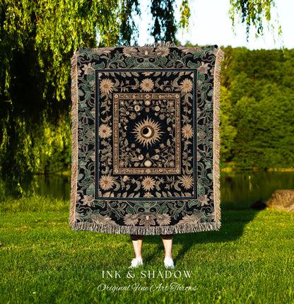 May include: A black woven tapestry throw blanket with a gold and green floral design. The center of the blanket features a large sun with a human eye in the center. The text 'INK & SHADOW Original Fine Art Throws' is printed below the blanket.