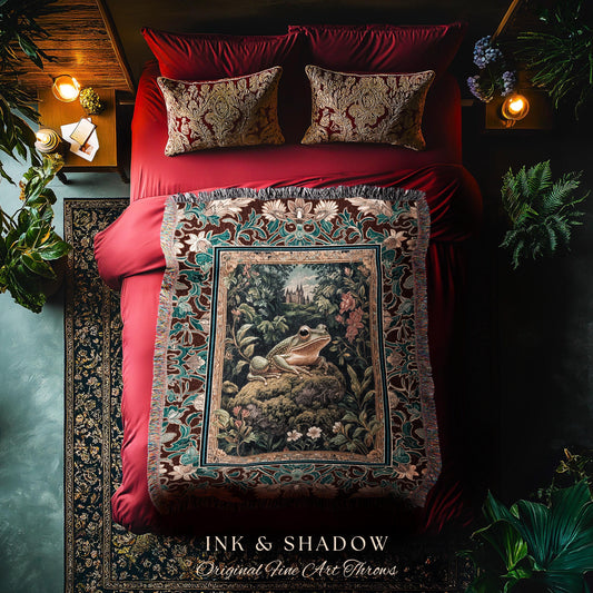 May include: A tapestry throw blanket with a dark red background and a green and brown floral pattern. The center of the tapestry features a green frog sitting on a rock in a forest setting. The tapestry has fringe around the edges. The text 'INK & SHADOW Original Fine Art Throws' is printed on the bottom of the tapestry.